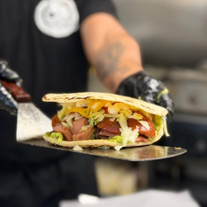 Una mixta con salchicha y repollo sostenida en la espátula